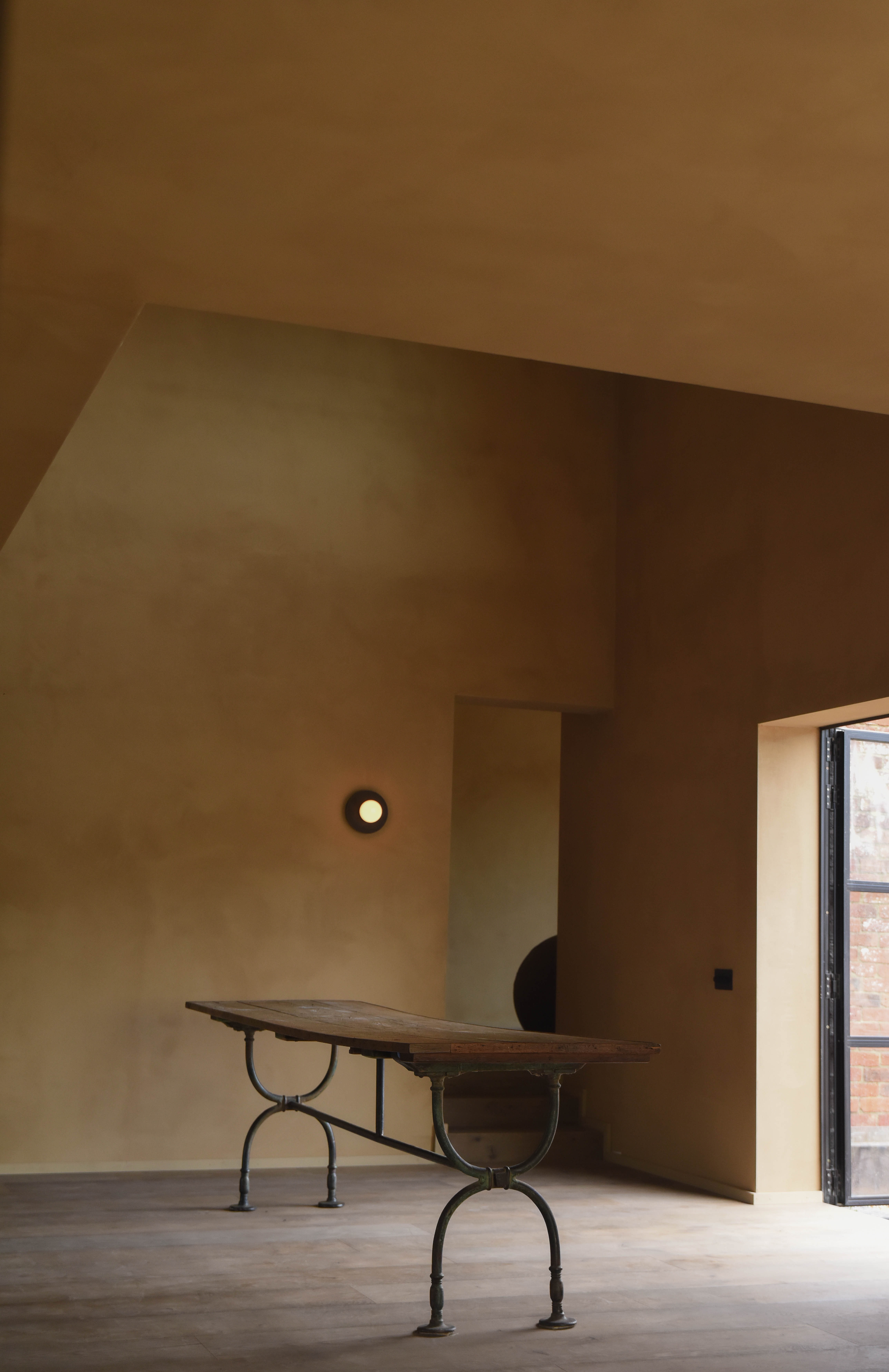 Long iron-based dining table against tall clay walls