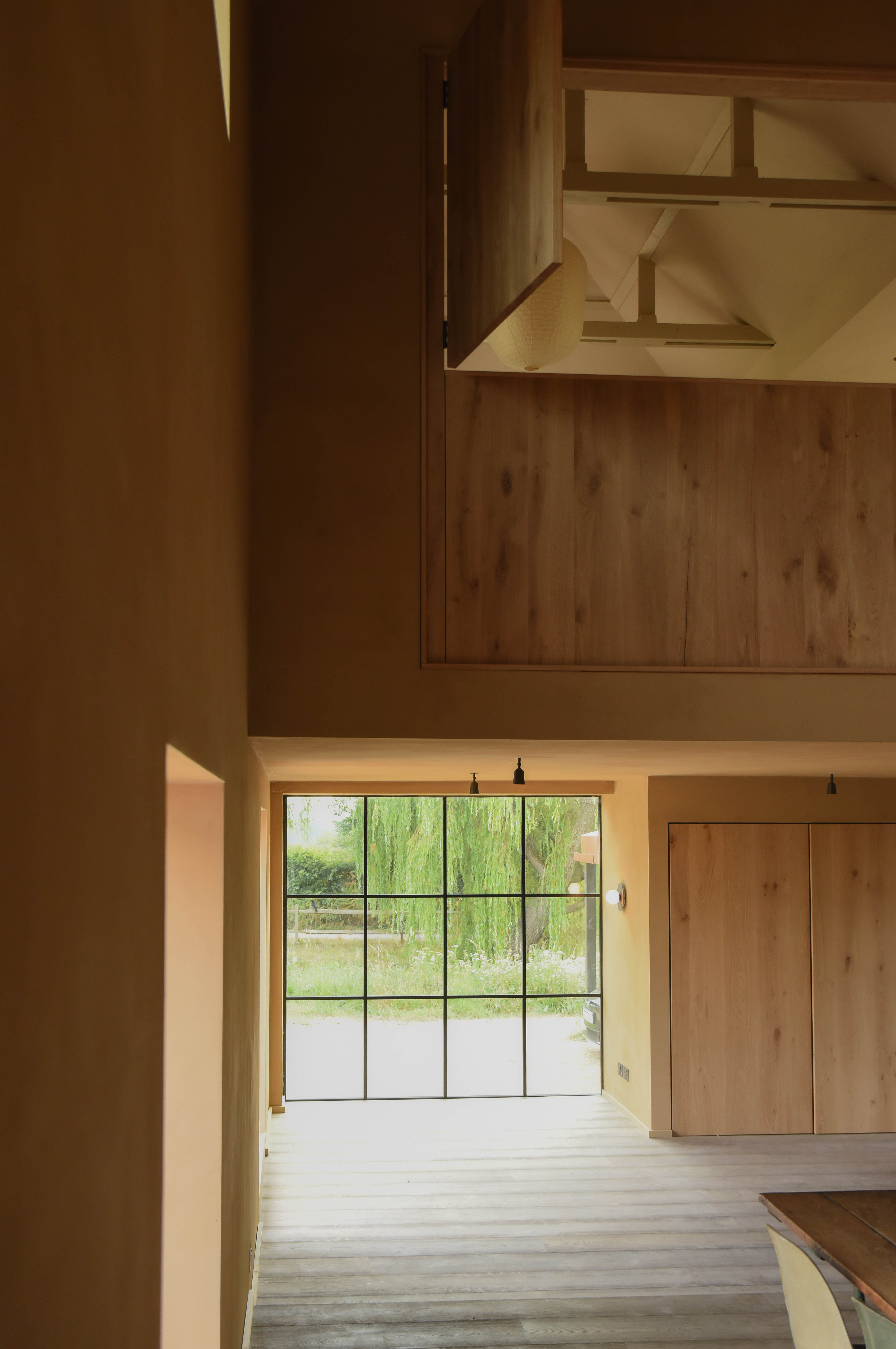 The double-height volume, oak mezzanine above and steel-framed window to the willow beyond