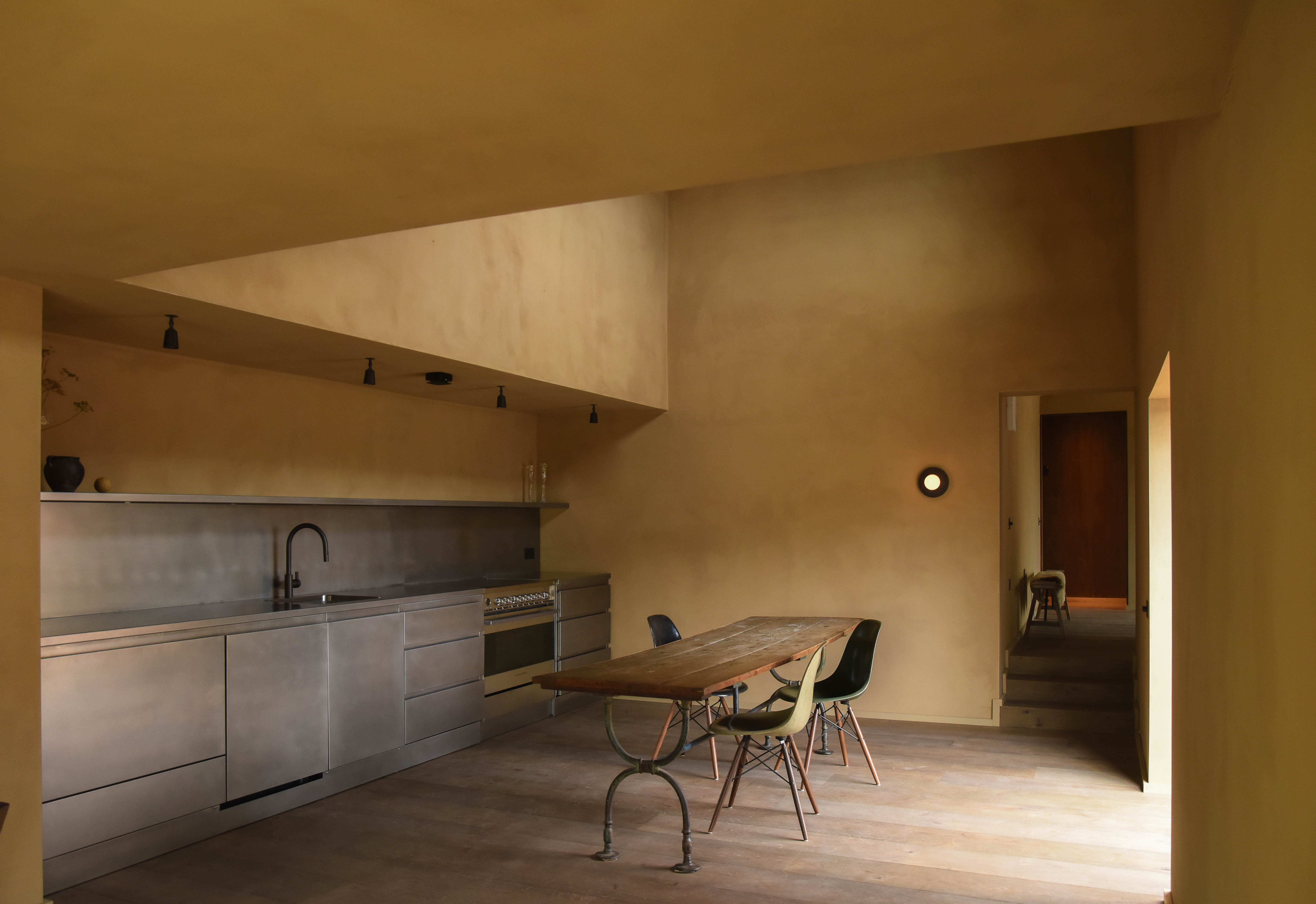 Stainless steel commercial kitchen and dining table beneath clay-plastered walls