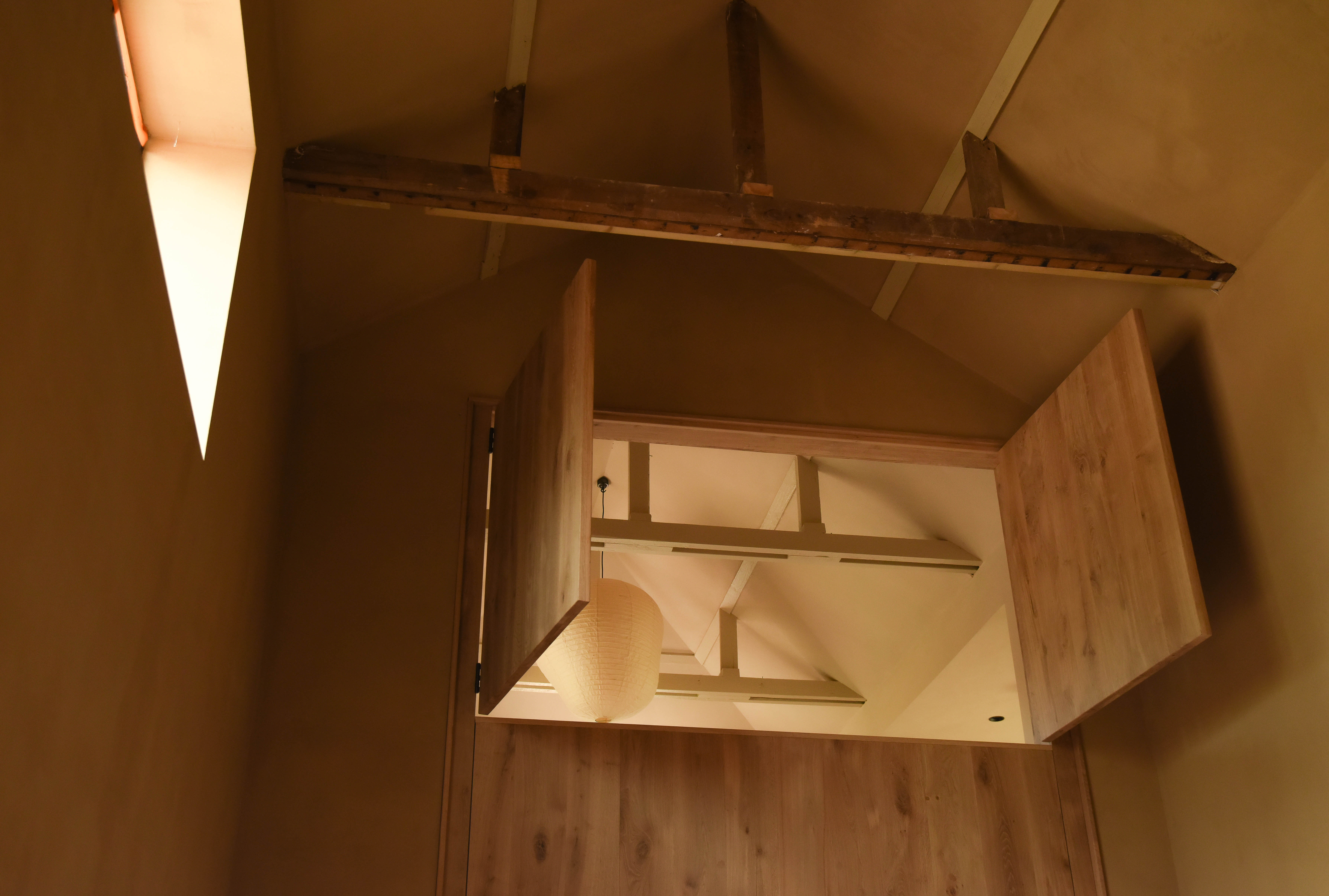 Looking up through the double-height space, oak shutters open to the apartment